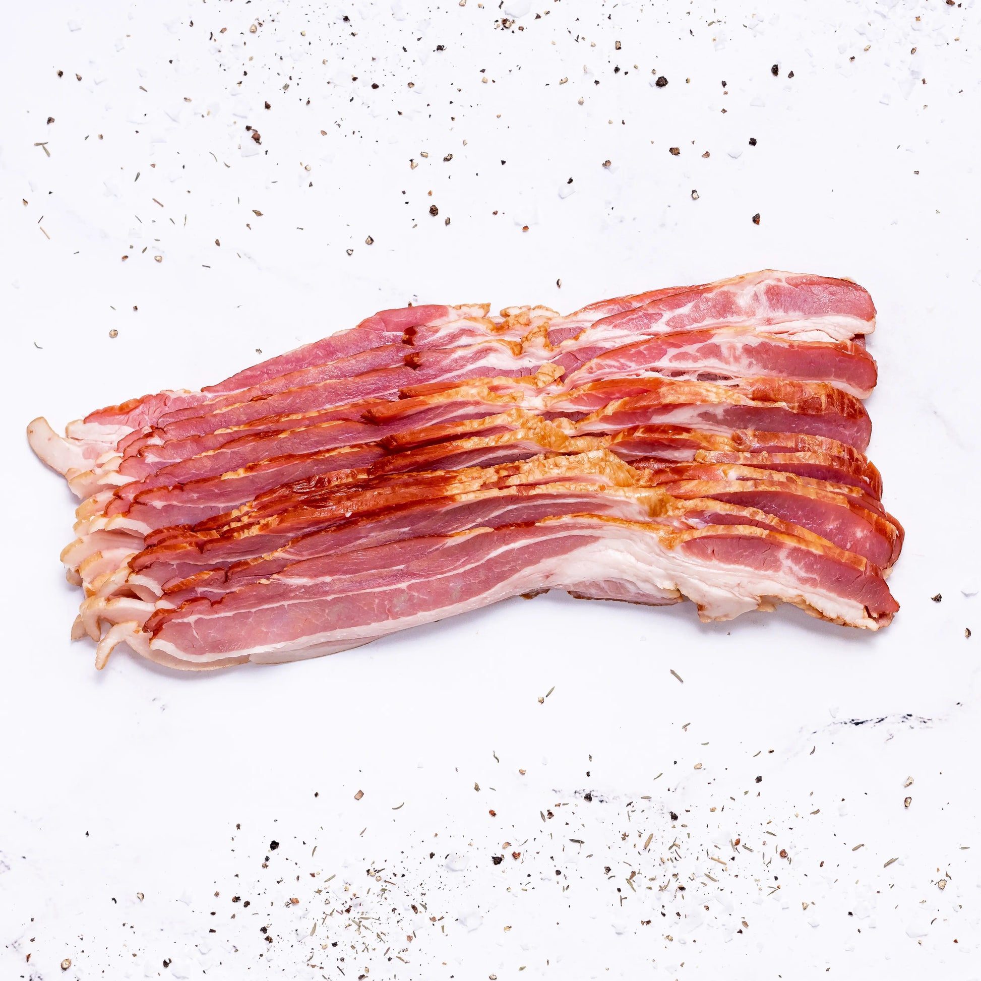 Several strips of Applewood Bacon are arranged neatly on a white surface, surrounded by scattered black pepper and seasoning.