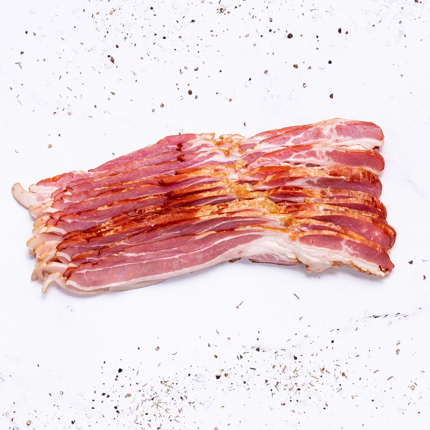 Several strips of Applewood Bacon are arranged neatly on a white surface, surrounded by scattered black pepper and seasoning.