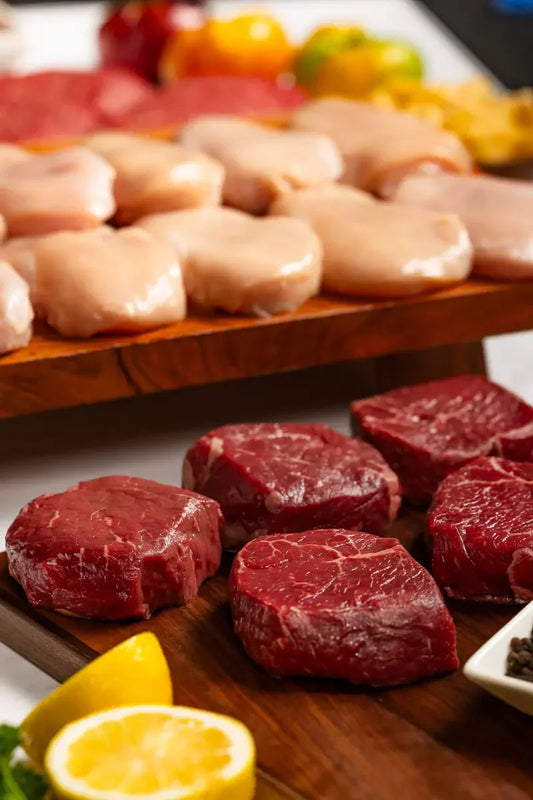 The Family Feast Bundle features raw beef steaks and boneless chicken breasts sourced from local American family farms. Beef is in the front, chicken in back for a fresh, appetizing display.